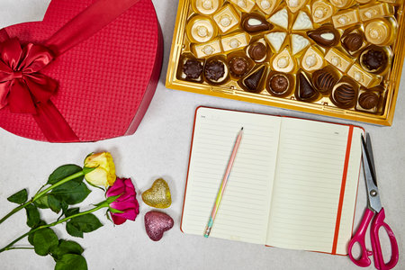 chocolate pieces from various type in box for valentine's day with red heart shaped box and roses flowers and empty notebookの写真素材
