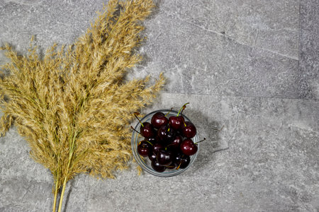 sweet cherry fruits in ceramic bowl with golden reeds plants on gray grunge backgroundの写真素材
