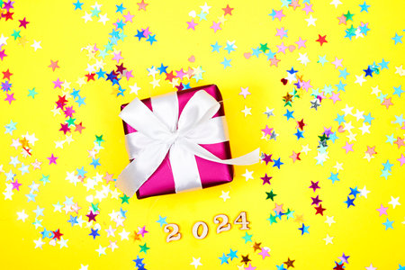 happy new year 2024 background new year holidays card with bright lights, gift box with stars confetti on yellow backgroundの写真素材