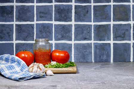 Fresh Garlic near to tomato sauce in glass bottle with parsley on cutting board with wooden spoon on grunge gray floorの写真素材