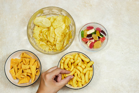 bowls of different chips and jelly candies on grunge background and hand holding one piece of chipsの写真素材