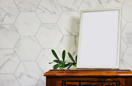 empty picture frame mockup on wooden table and ruscus plants. Elegant working space, home office concept. Scandinavian interior designの写真素材