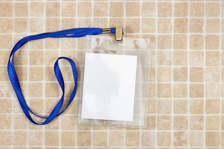 Blank badge mockup. Plain empty name tag mock up on mosaic tiles. Name tag with blue ribbon and transparent plastic paper holder. Badge clipping path. Corporate designの写真素材