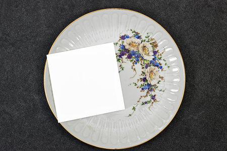 Wedding invitation card mockup above gray floral ceramic plate  on gray background. Blank card mockupの写真素材