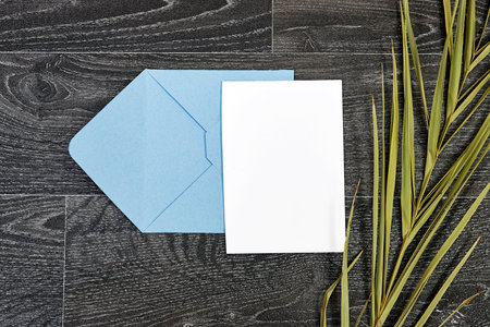 Envelope and palm leaf on wooden background. Flat lay.