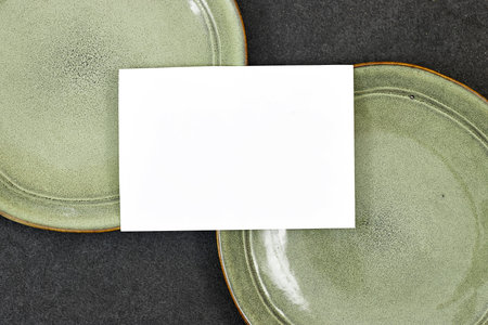 Wedding invitation card mockup above green ceramic plate on gray background. Blank card mockupの写真素材