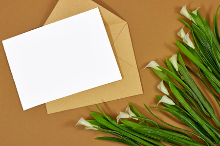 Blank greeting card, flyer or invitation card mockup  and brown craft envelope with calla lilies, Valentines or women's day heart on brown backgroundの写真素材