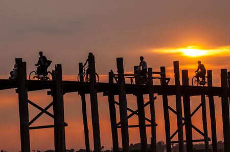 Mandalay,Myanmar-March 16,2011 : Unidentified Myanmar  People with bicycle on U-Bein bridge in sunset in Mandalay, Myanmar. The U-Bein bridge is the longest teak bridge in the world, 1.2km lenght is spanning the Taungthaman Lake. It is 200 years old.のeditorial素材