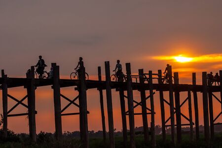 Mandalay,Myanmar-March 16,2011 : Unidentified Myanmar  People with bicycle on U-Bein bridge in sunset in Mandalay, Myanmar. The U-Bein bridge is the longest teak bridge in the world, 1.2km lenght is spanning the Taungthaman Lake. It is 200 years old.のeditorial素材