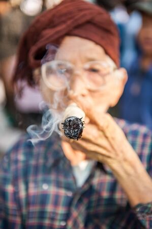 BaganMyanmarMarch 182011: An unidentified woman smoking a cheroot cigar in market in bagan Myanmar . A cheroot is a cigar made principally by dried fruits and little bit of tobacco.のeditorial素材