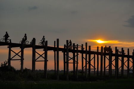 Mandalay,Myanmar-March 16,2011 : Unidentified Myanmar  People with bicycle on U-Bein bridge in sunset in Mandalay, Myanmar. The U-Bein bridge is the longest teak bridge in the world, 1.2km lenght is spanning the Taungthaman Lake. It is 200 years old.のeditorial素材