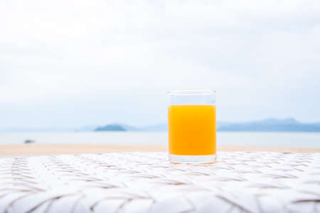 A glass of orange juice on white table next to the beach restaurantの写真素材