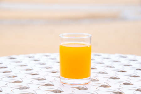 A glass of orange juice on white table next to the beach restaurantの写真素材