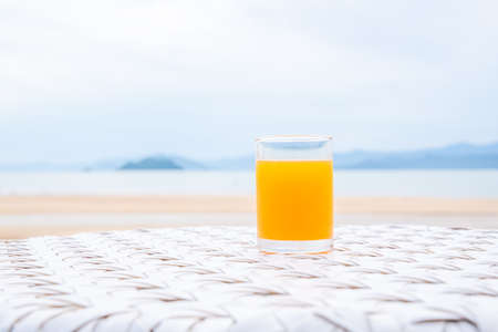 A glass of orange juice on white table next to the beach restaurantの写真素材