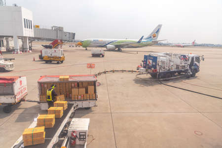 Bangkok, Thailand- January 24 2021 : Airline crew loads checked baggage into airplane cargo and refueling of the aircraft at Don Mueang airport (DMK) in Bangkok ,Thailand.のeditorial素材