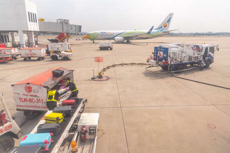 Bangkok, Thailand- January 24 2021 : Airline crew loads checked baggage into airplane cargo and refueling of the aircraft at Don Mueang airport (DMK) in Bangkok ,Thailand.のeditorial素材