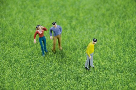 Mini toy man and woman looking at an oldman standing on a grass fieldの写真素材