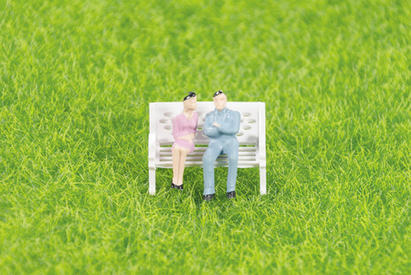 Mini toy man and woman sitting on a chair on a grass fieldの写真素材