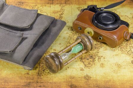 bag hourglass and pocket camera on a old world mapの写真素材