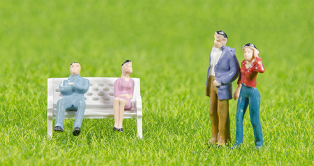 Mini toy man and woman sitting on a chair with other couple on a grass fieldの写真素材