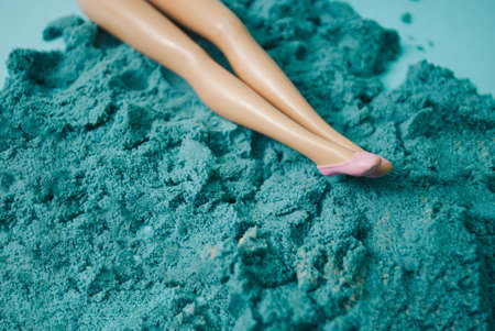 Doll's legs in pink shoes on blue beach sand. Creative summer fun composition.の写真素材
