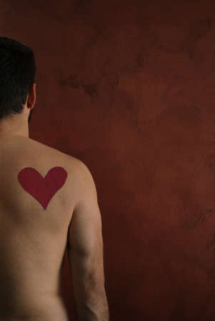 Red heart painted with lipstick on man's back on bronze dramatic background. Creative concept, side view.の写真素材