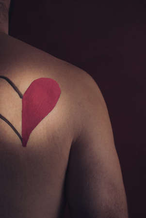 Symbol of love heart painted with lipstick on man's back on dark dramatic background. Creative concept, side view.の写真素材