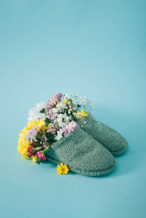 Spring colorful flowers growth from slippers on turquoise background. Creative concept, side view.の写真素材