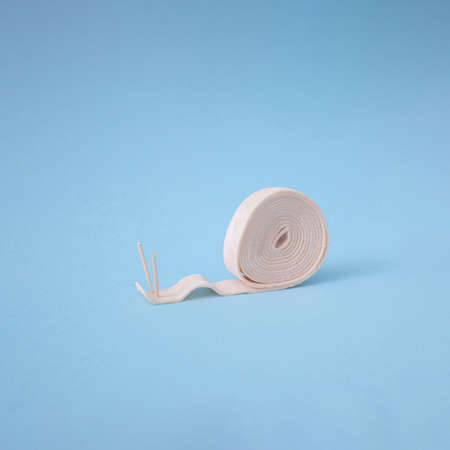 Roll of pastel pink bubble gum with two toothpicks on light blue background look like snail. Side view, interesting concept.の写真素材