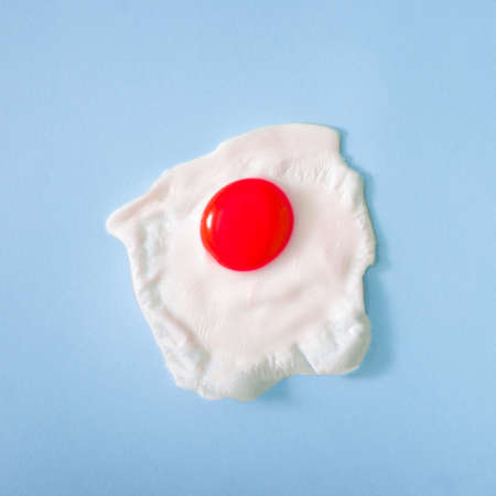 Fried egg with coloured red yolk isolated on pastel blue background. Top view, food cooking photo. Creative design. Flat lay.の写真素材