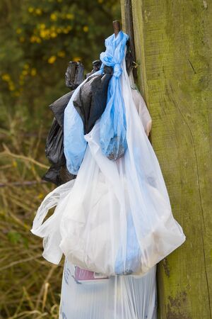 several plastic bags of rubbish hung on a wooden fence postの写真素材
