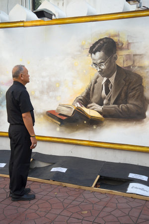 BANGKOK. THAILAND - DECEMBER 11, 2016: Elderly Thai in black mourning clothes standing near the wall with the image of King Bhumibol Adulyadejのeditorial素材