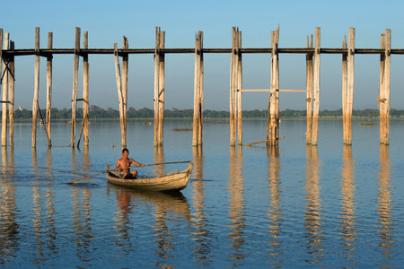 MANDALAI, MYANMA - DECEMBER 20, 2016: A burmese man swims on a traditional wooden boat at the old U Bein bridge  on the  Thaungthaman Lakeのeditorial素材