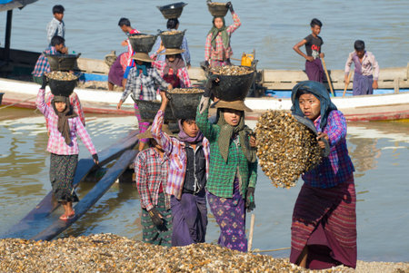 BAGAN, MYANMAR - DECEMBER 23, 2016: Burmese girls unload the barge with the river gravel