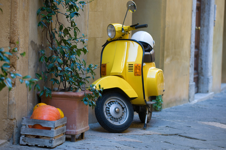 Box with orange pumpkins, green plant and yellow scooter at the wall of the old houseの写真素材