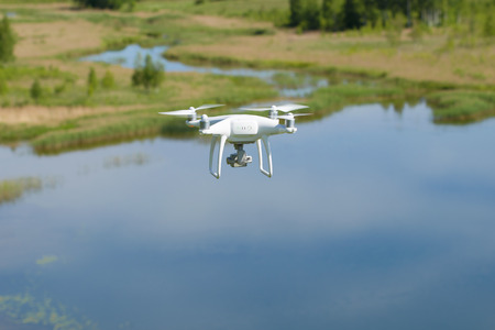 A flying white quadrocopter over a summer lakeの写真素材
