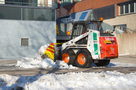 TURKU, FINLAND - FEBRUARY 23, 2018: A small wheel loader removes snow on the city sidewalkのeditorial素材