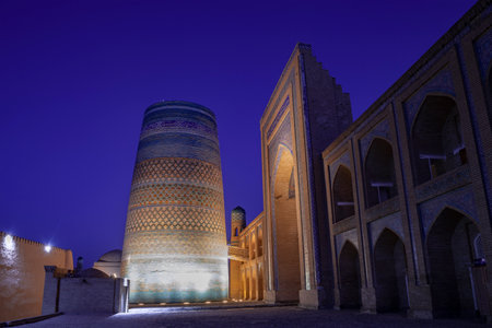 KHIVA, UZBEKISTAN - SEPTEMBER 05, 2022: Ancient Kalta-Minor minaret and portal of Muhammad Amin-khan madrasah in night landscapeのeditorial素材