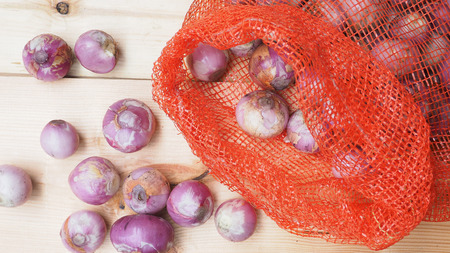 Red onion peeled crop photo, peeled zoom in and prepared for sale in market, In a mesh bag red color on wooden, Photo focus select at center.の写真素材