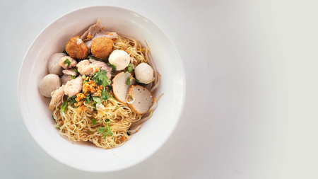 Egg noodle dry Asian food, Have pork ball, fish, parsley, green onions, sliced, soup, shrimp dumplings in white plastic bowls isolate on white background has copy space.の写真素材
