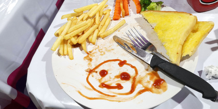 Breakfast or lunch the boy create to drawn tomato sauce cartoon smiling face on his plate white color.の写真素材