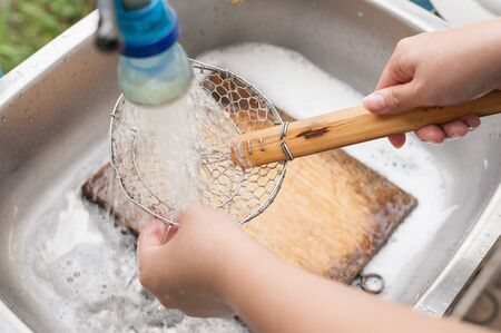 two hands washing colander and wooden chopping board in the metal sinkの写真素材