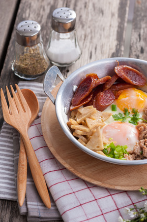 Vietnamese style fried egg in pan with white pork sausage, Chinese sausage, and pork on wood table.の写真素材