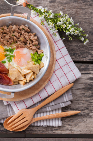 Vietnamese style fried egg in pan with white pork sausage, Chinese sausage, and pork on wood table.の写真素材