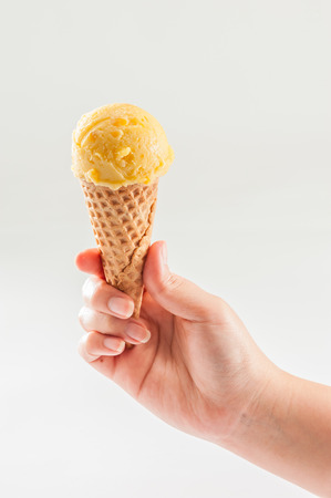 A woman hand holding Mango ice cream scoop on coneの写真素材