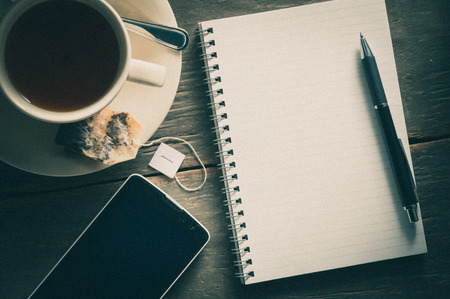 Small notepad with a cup of tea, pen, pencil and cellphne on rustic wood background with film filter effectの写真素材