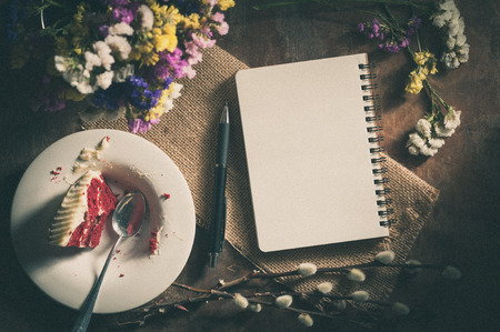 Small notepad with pen, pencil and bits of red velvet cake on rustic wood background with film filter effectの写真素材