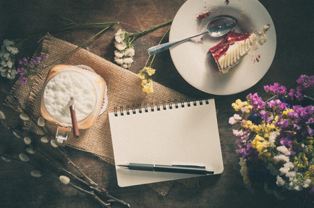 Notepad with pen, a glass of Thai tea and bits of red velvet cake on rustic wood with film filter effectの写真素材