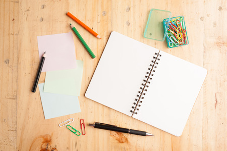 Notebook and sticky paper, paper clip, color pencil, and pen on wood tableの写真素材