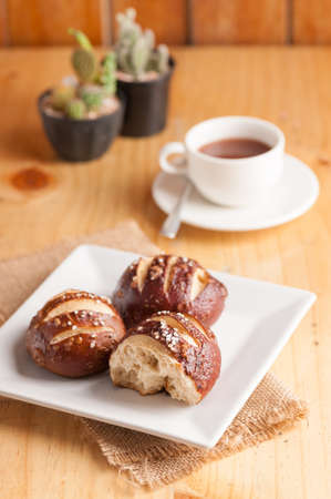 Freshly baked soft pretzel with generous sprinkling of coarse salt on white dish and a cup of hot chocolate in backgroundの写真素材